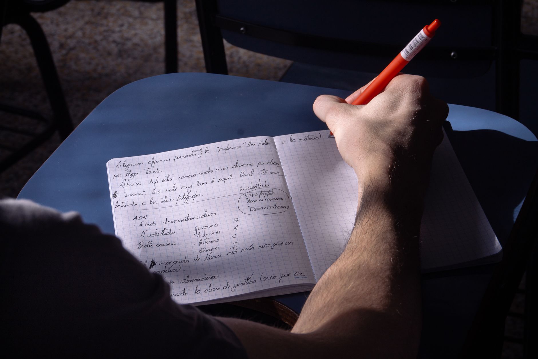 A student takes notes in a classroom. Natural lighting highlights the writing process.